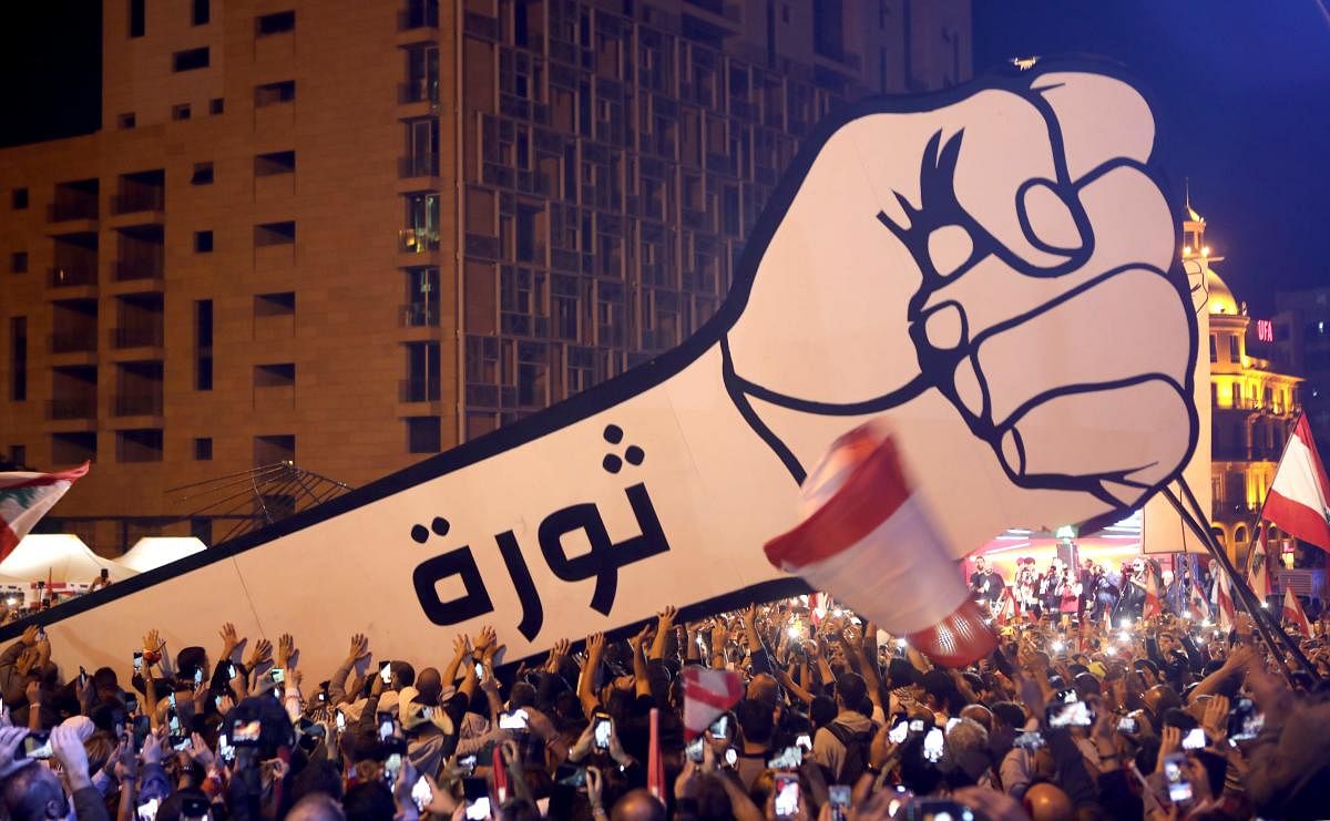 Lebanese demonstrators raise a new giant sign of a fist that bears the Arabic word "revolution" on it, in the Lebanese capital Beirut's Martyr's Square on November 22, 2019, after the sign was burnt overnight by unknown perpetrators.