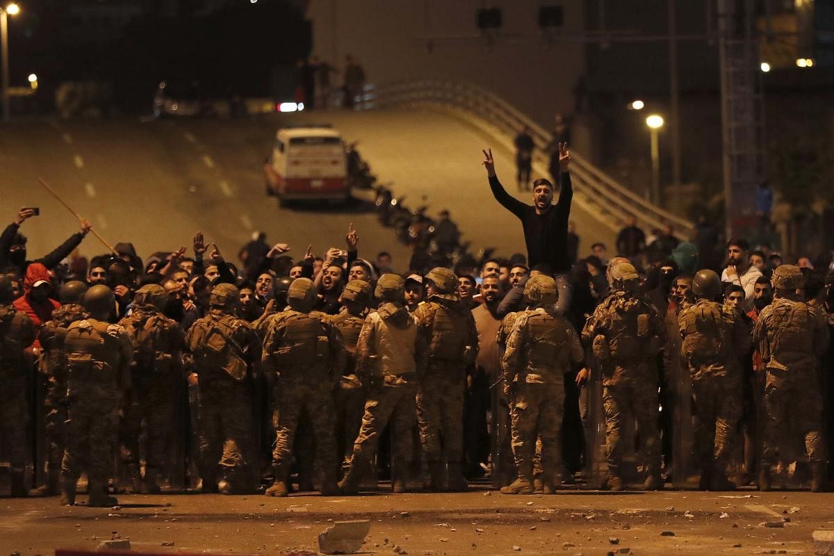 Supporters of the Shiite Hezbollah and Amal Movement groups shout slogans as they stand in front of Lebanese army soldiers after a clash erupted between the anti-government protesters and them, in Beirut, Lebanon. (AP Photo)
