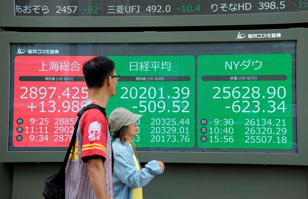 Pedestrians walk in front of an electric quotation board displaying the numbers oF the Nikkei 225 index at the Tokyo Stock Exchange (C), the Shanghai Stock Exchange (L) and New York Dow (R) in Tokyo on August 26, 2019. (AFP Photo)
