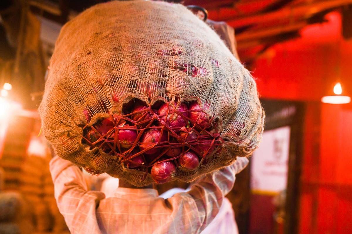 A labourer carries a sack of onions on is head as he makes his way in a market in Kolkata on November 29, 2019. (AFP Photo)
