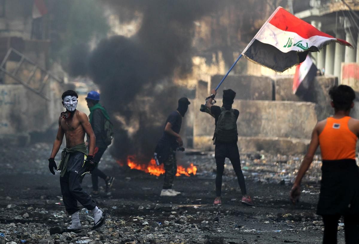 An Iraqi anti-government protester waves a national flag close to a concrete barricade amidst clashes with security forces along the capital Baghdad's Rasheed street. Photo by AFP
