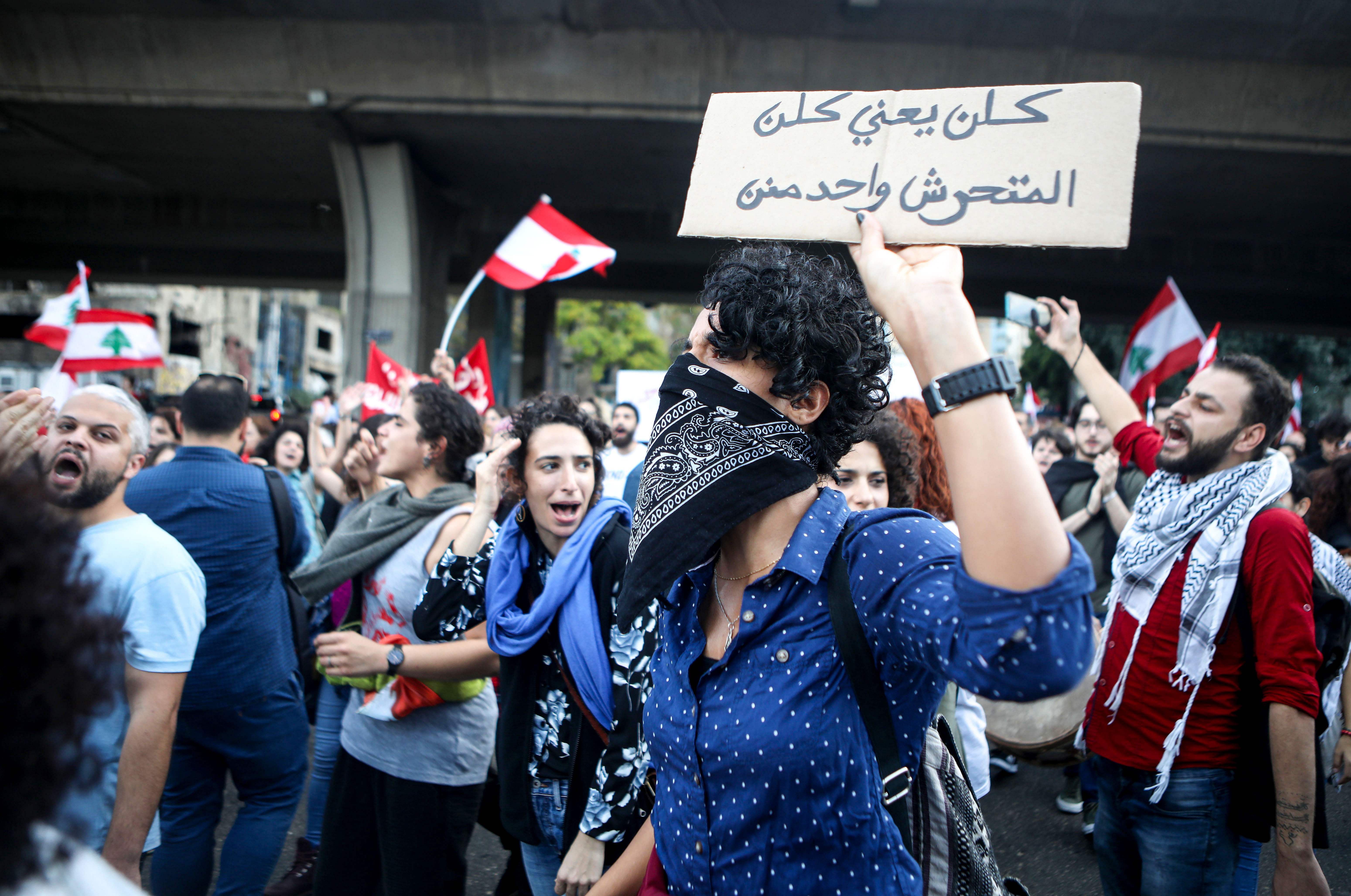A Lebanese anti-government protester holds up a sign reading "all means all, including harassers", during a demonstration march on the former demarcation line separating Beirut. (AFP Photo)