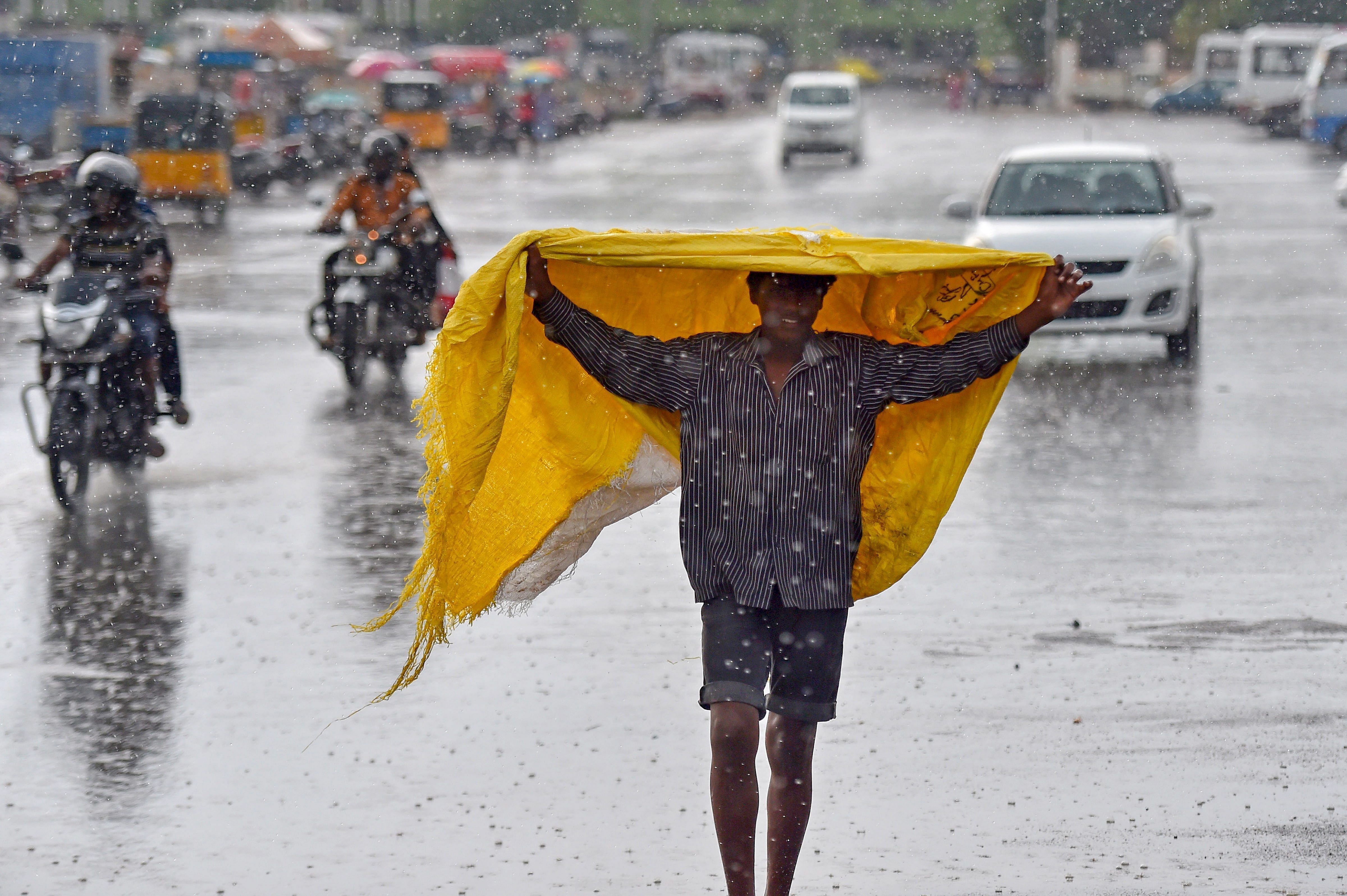 A boy covers himself with a plastic sheet as rain lashed several parts of the city, near Marina beach in Chennai. (PTI Photo