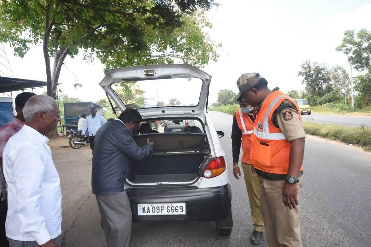 Police and poll officials inspect a car, intercepted at a checkpost, under Hunsur Assembly segment in Mysuru district, recently. dh photo
