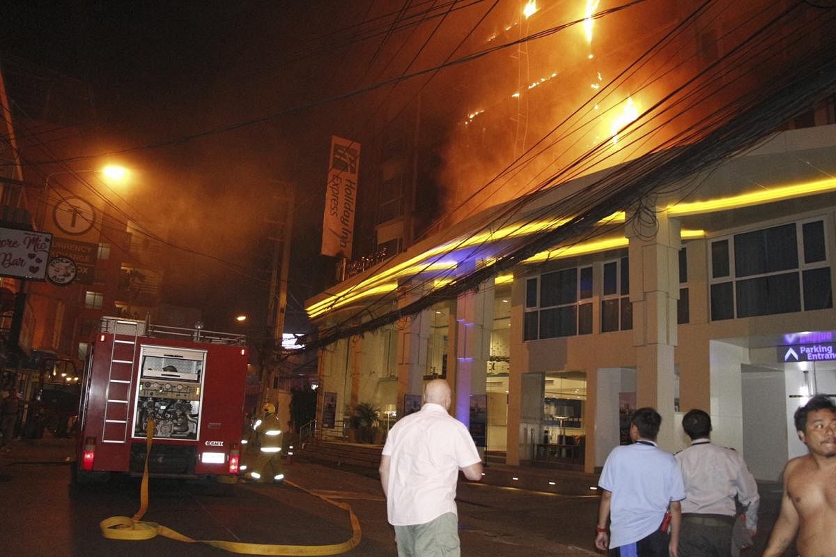 Tourists watch as a fire rages on the upper floors at the Holiday Inn Express Hotel in Pattaya. Photo by PTI.