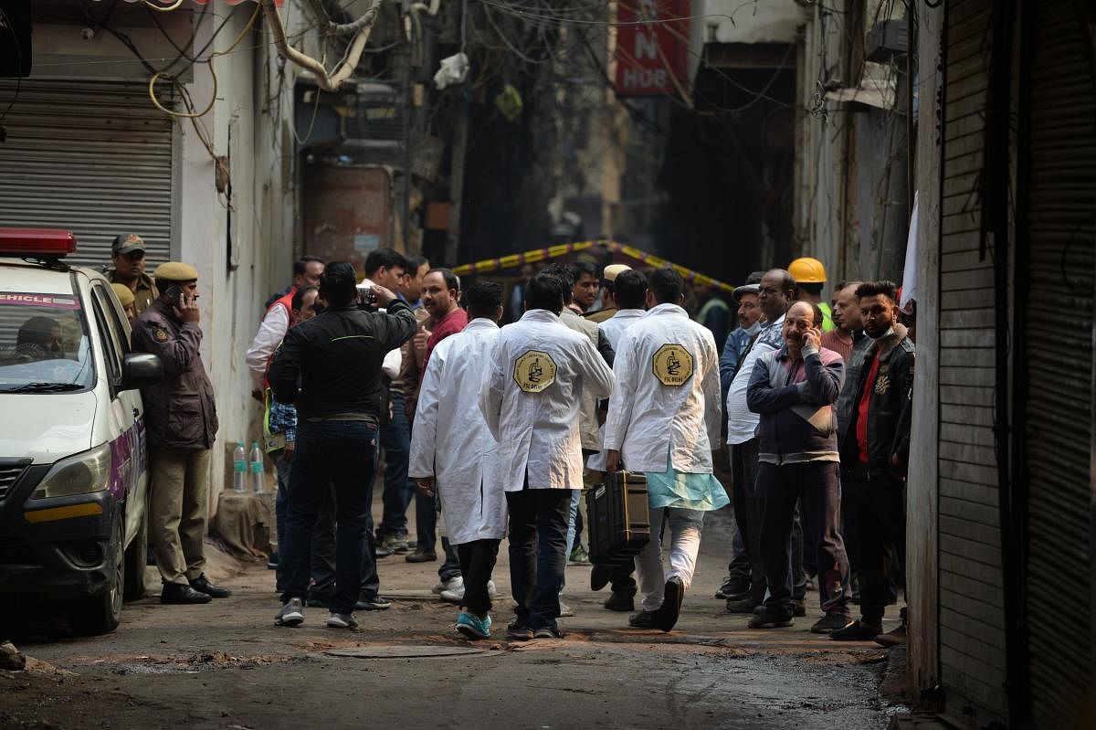 A forensics team walks along a street leading to a factory site where a fire broke out, in Anaj Mandi area of New Delhi. AFP
