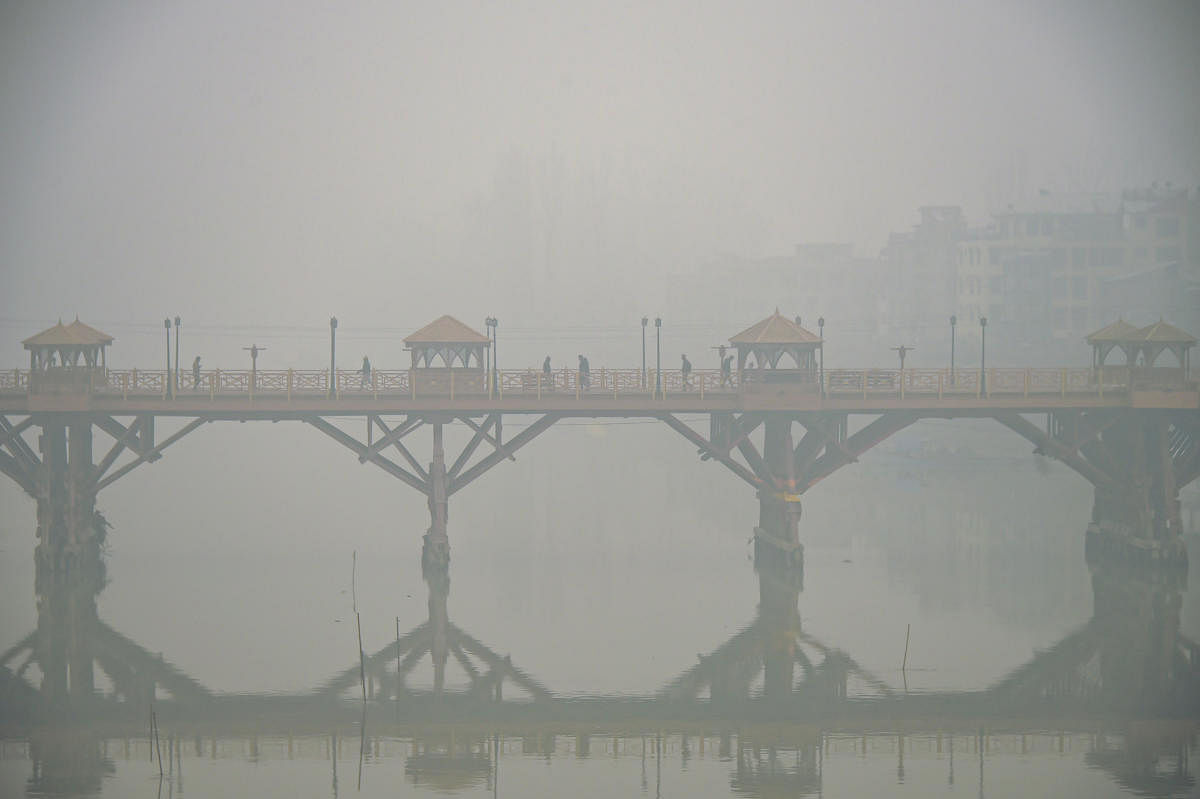 Pedestrians cross a bridge on a cold, foggy morning, in Srinagar. PTI