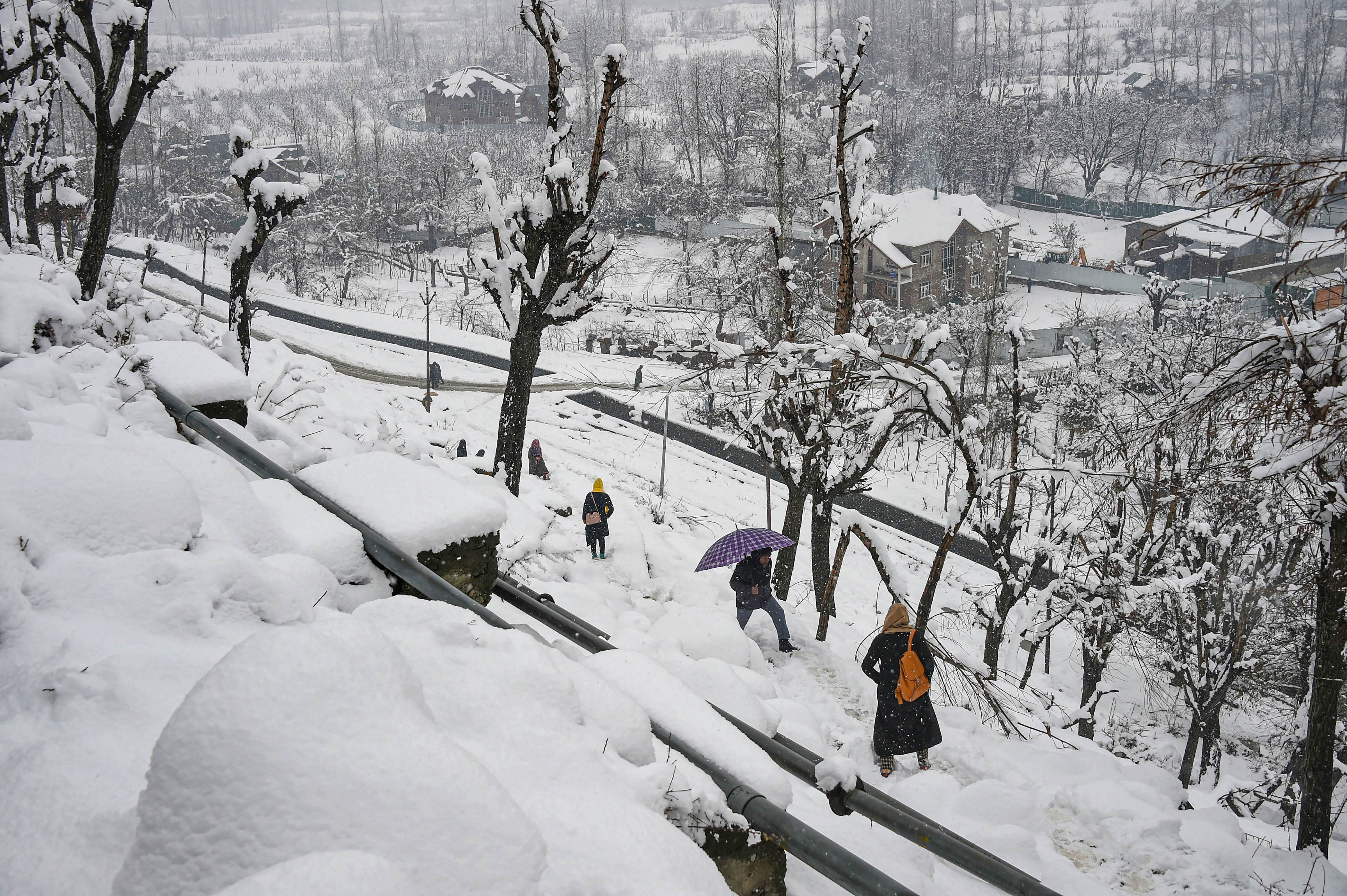 People on a snow-covered path to climb up hill during snowfall, on the outskirts of Srinagar. (PTI Photo)