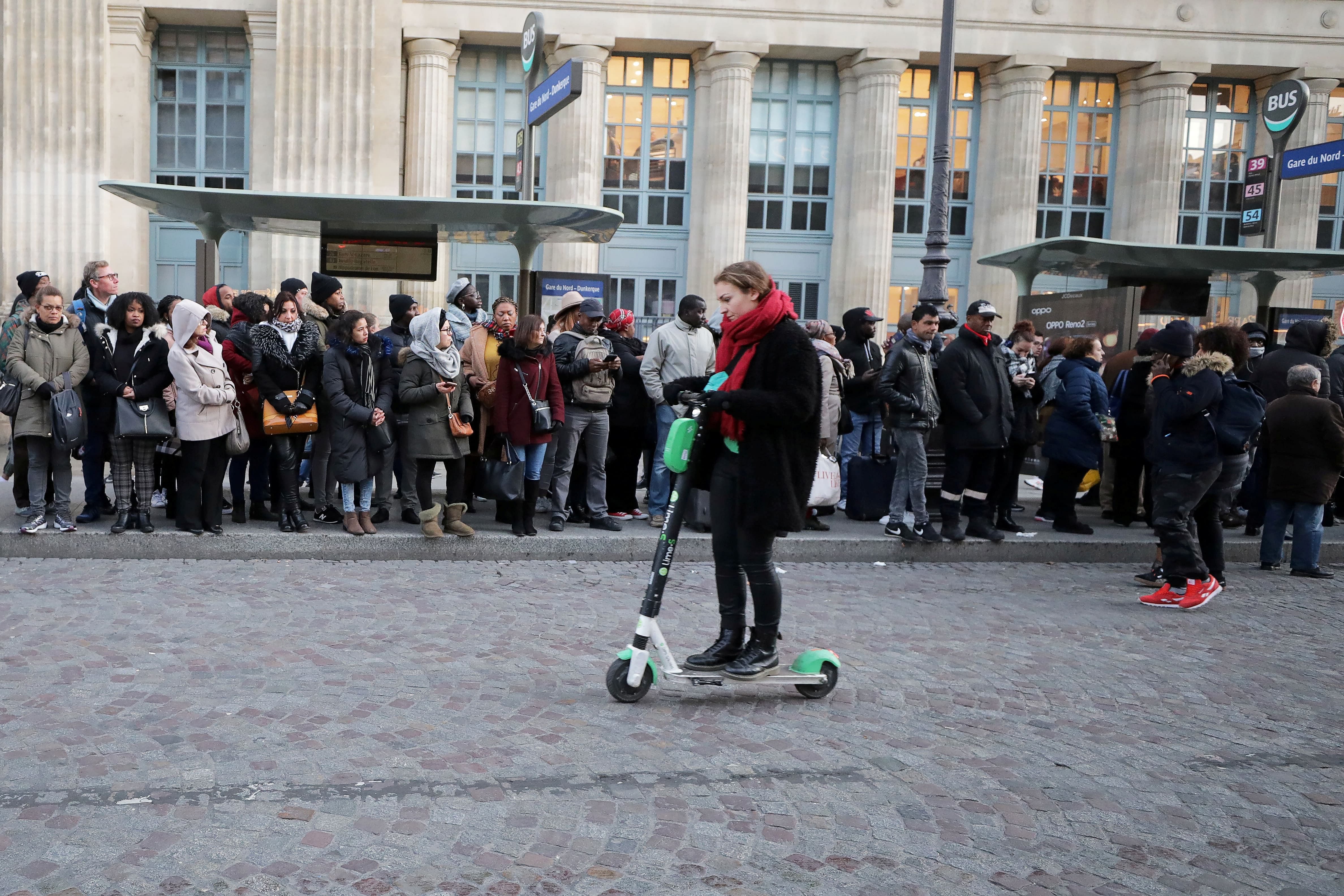 A woman rides a scooter past people waiting at bus stops at Gare du Nord station during strikes in Paris, France, December 10, 2019. (Reuters Photo)