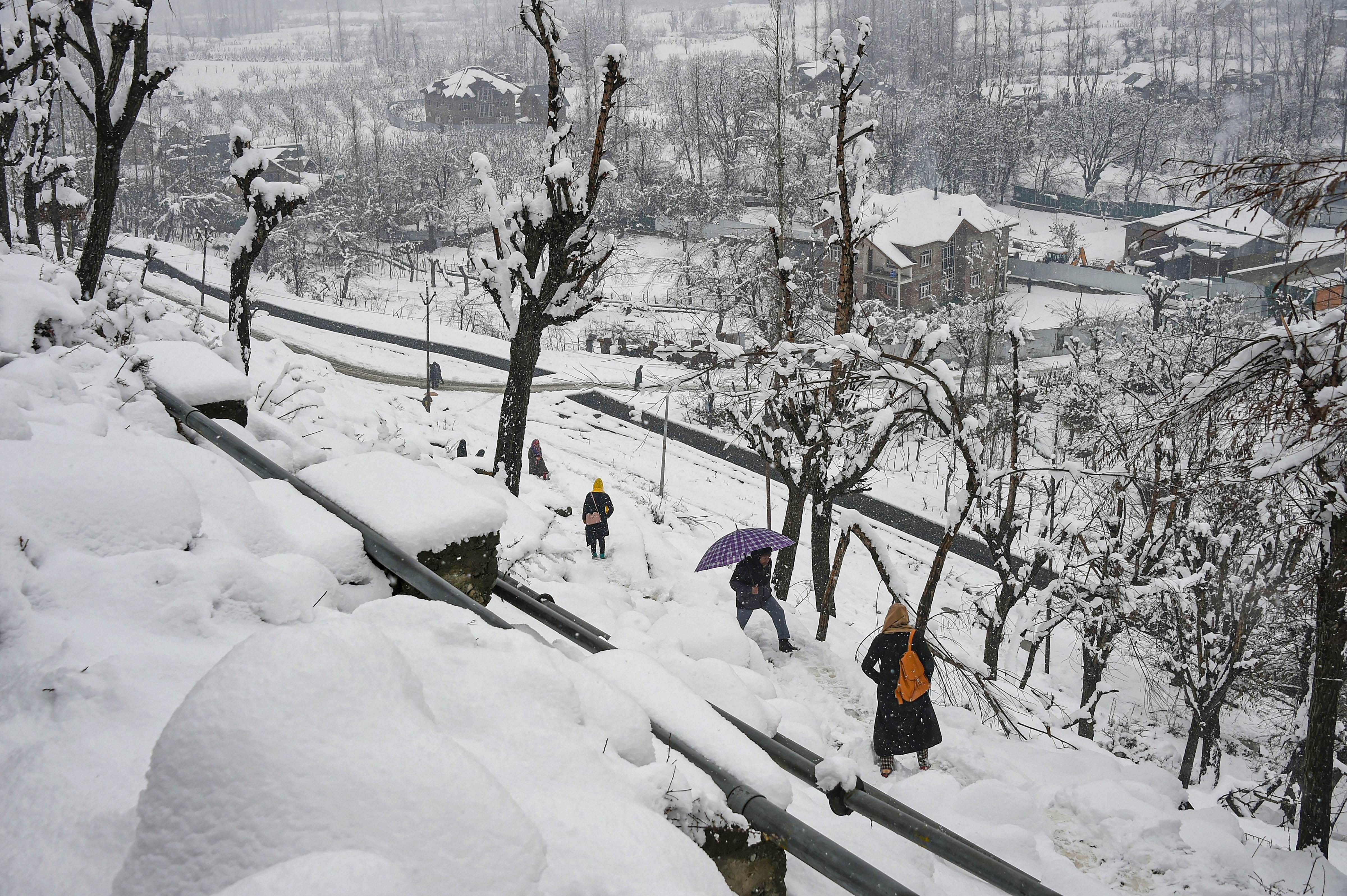 People on a snow-covered path to climb up hill during snowfall. (PTI Photo)