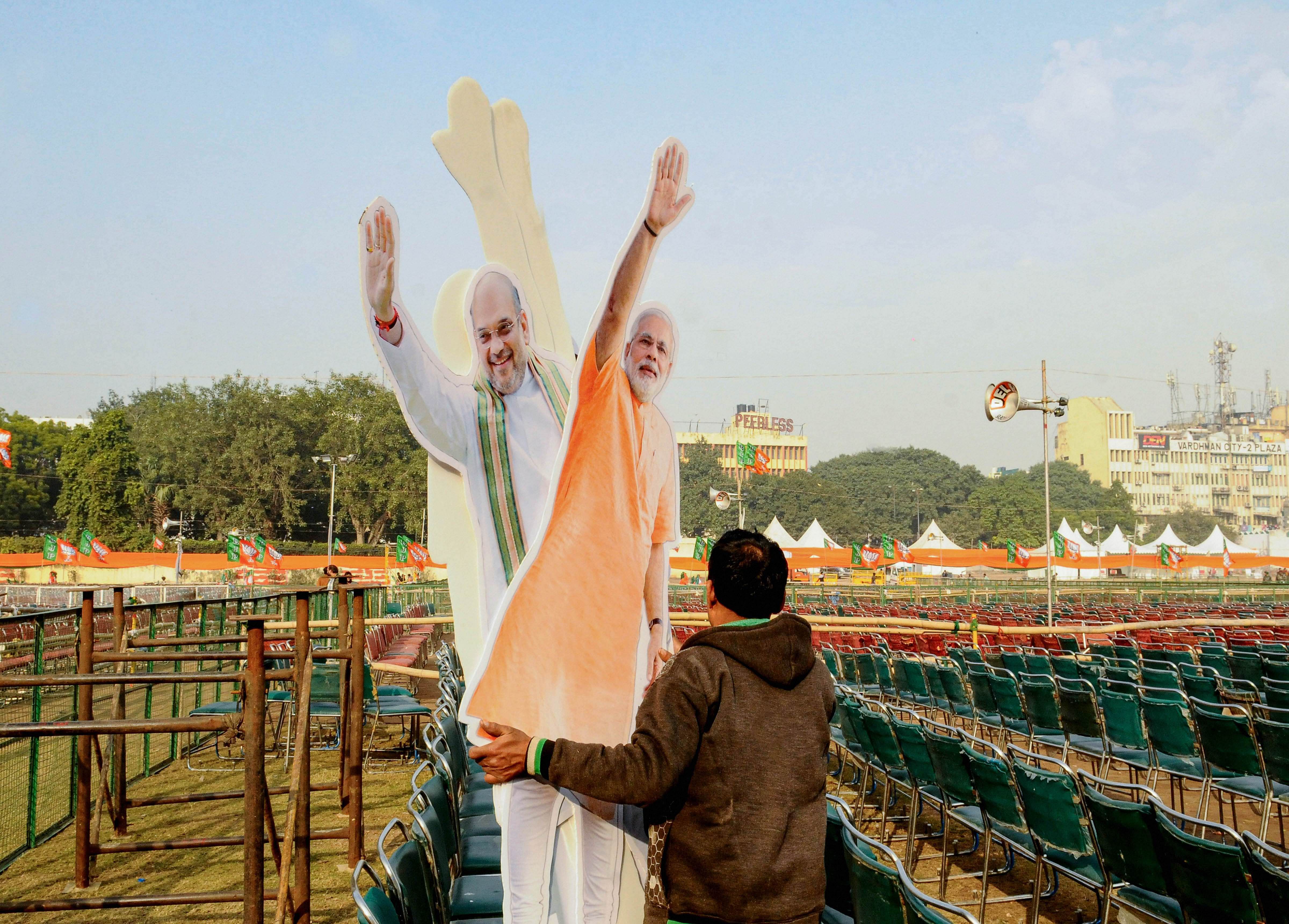 A workers carries cut-outs of Prime Minister Narendra Modi and Union Home Minister Amit Shah on the eve of  BJP rally at Ramlila Maidan in New Delhi. (PTI Photo)