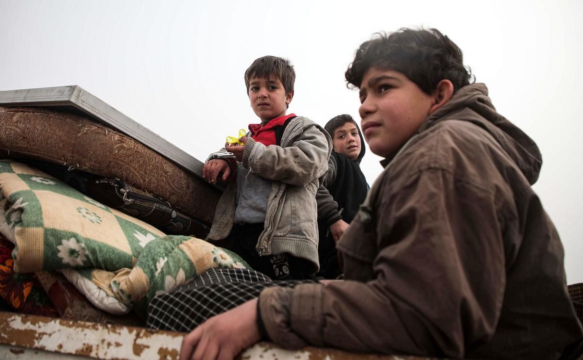 Syrian children look on while riding in the back of a truck as part of a convoy of people from the south of Idlib province fleeing bombardment by the government and its allies on the northwestern region, heading northwards along a highway near Sarmada on December 22, 2019. (Photo by Aaref WATAD / AFP)
