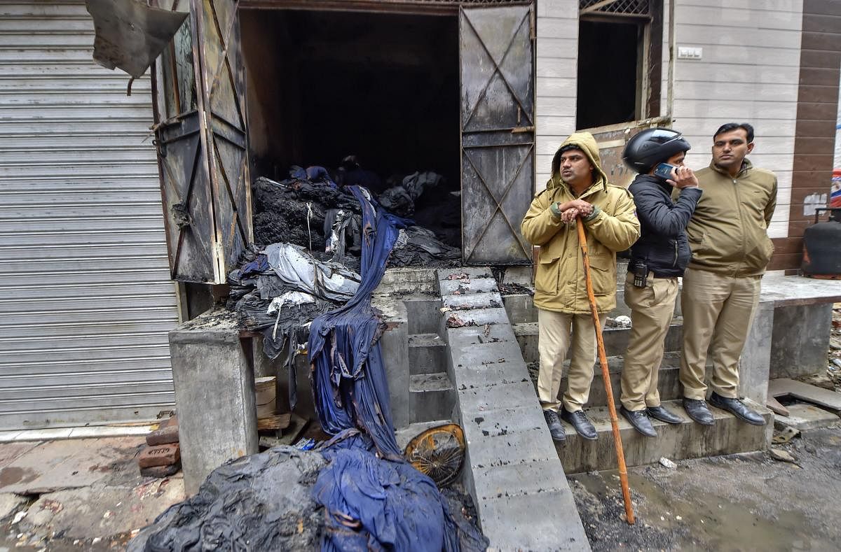Policemen stand outside the damaged three-storey residential-cum-commercial building where a fire broke out, in outer Delhi's Kirari area. (PTI photo)
