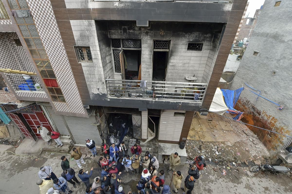 Police and media persons stand outside a three-storey residential-cum-commercial building where a fire broke out, in outer Delhi's Kirari area, Monday, Dec. 23, 2019. At least nine people, including three children, were killed in the incident. (PTI Photo)