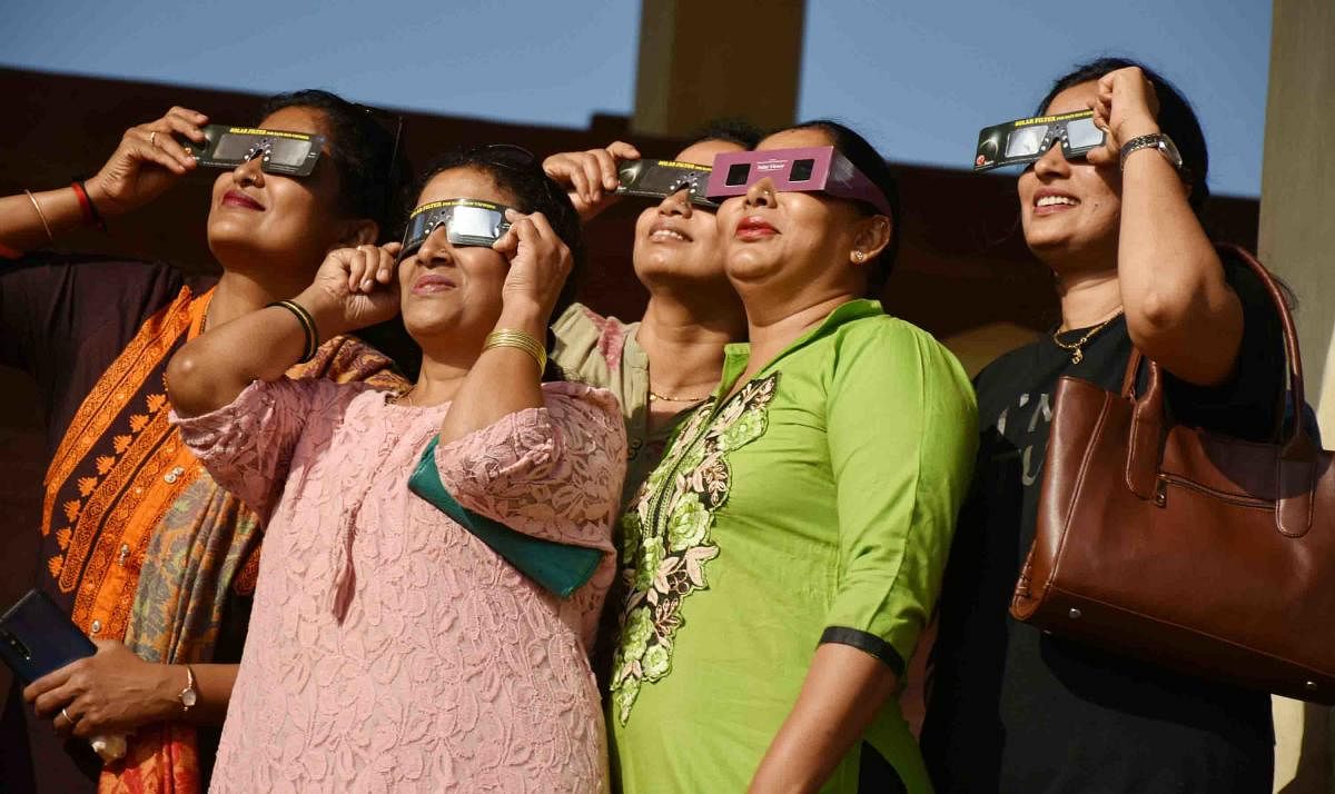 People watch solar eclipse using special glasses at General Thimmayya Circle in Madikeri on Thursday. DH Photo