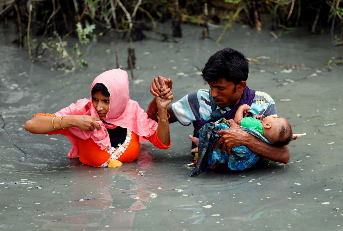 Rohingya refugees carry their child as they walk through water after crossing border by boat through the Naf River in Teknaf, Bangladesh. Photo/Reuters