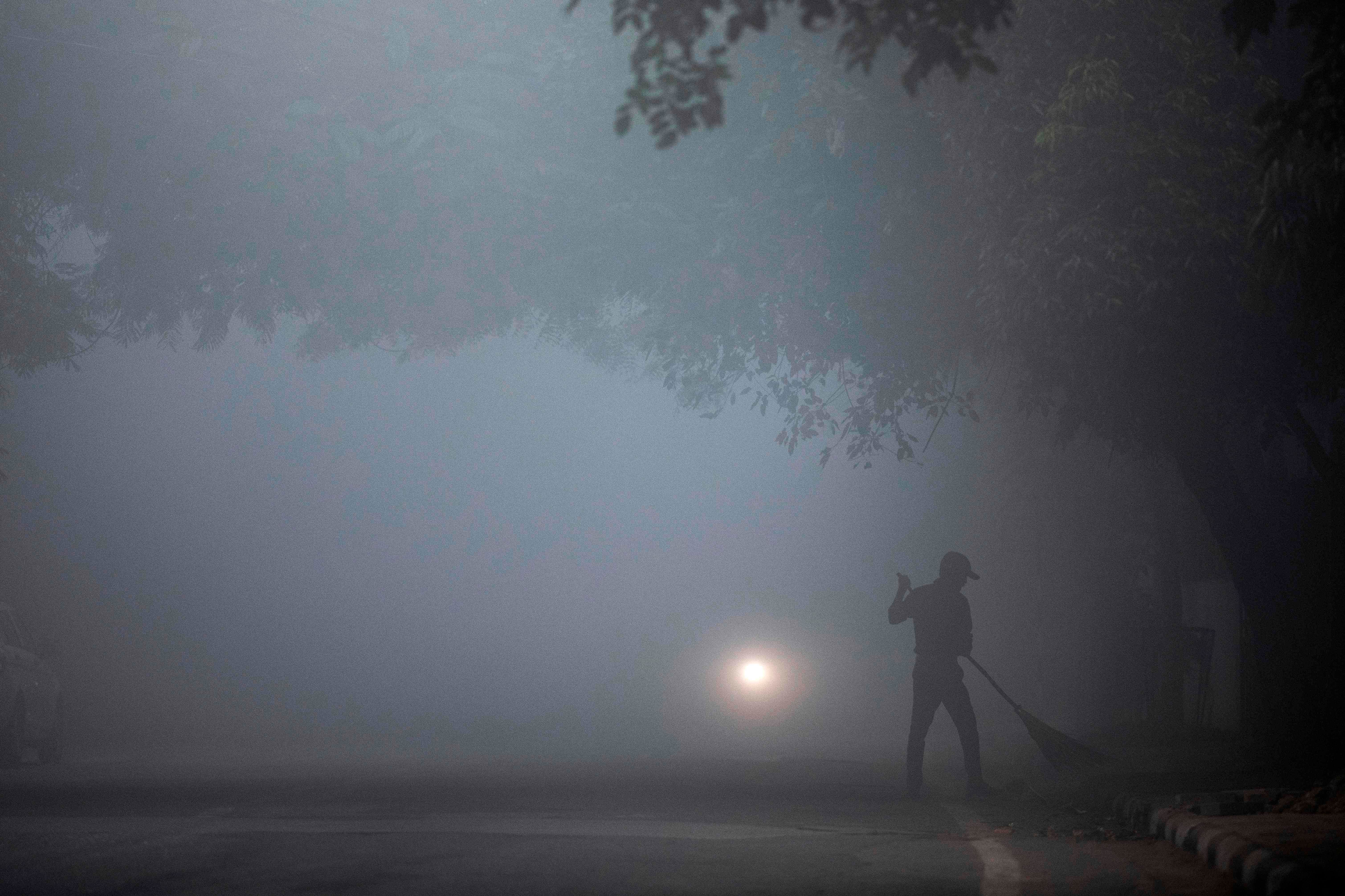 A man sweeps a street under heavy foggy conditions in New Delhi. (AFP Photo)