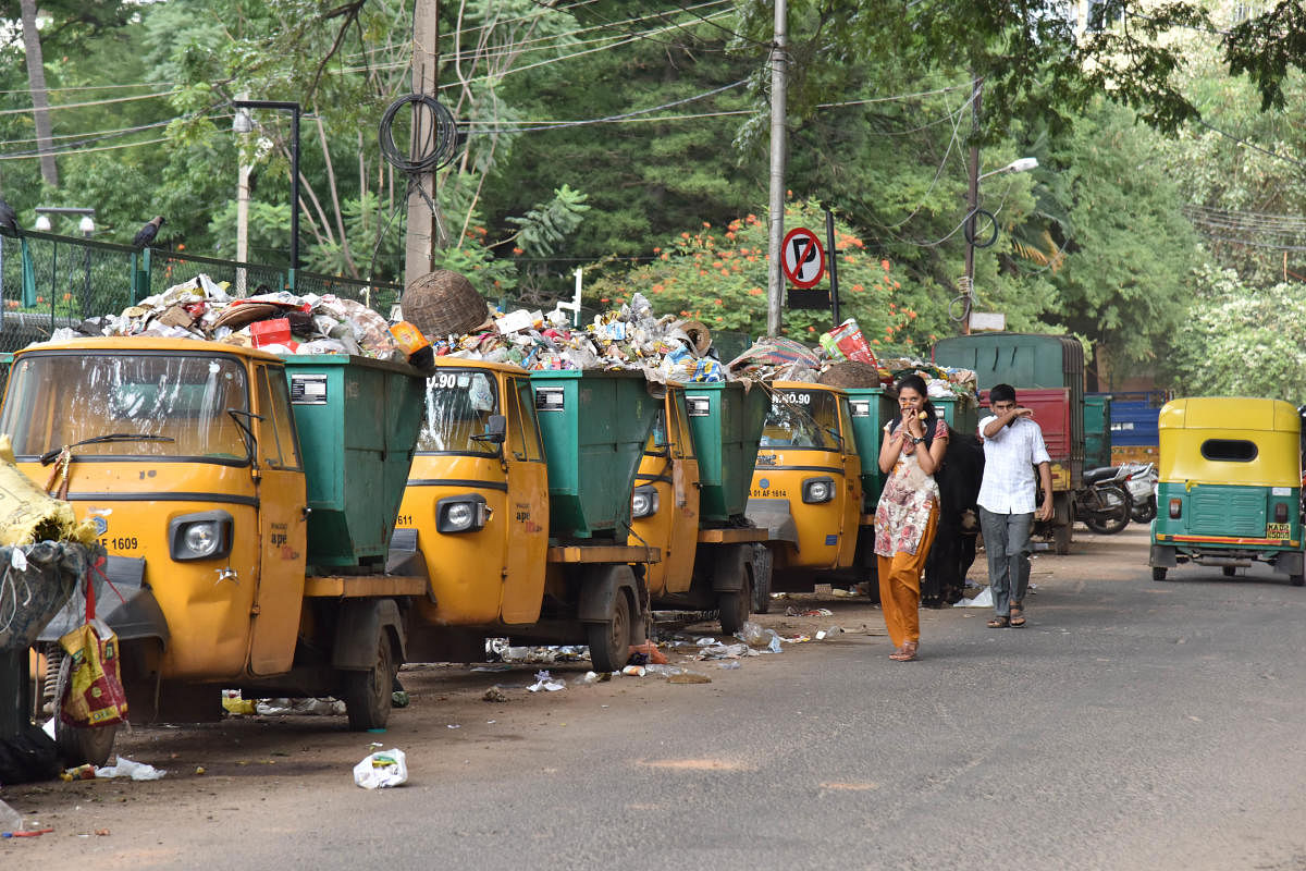 Pedestrians cover their nose and walks near lined up garbage filled BBMP tippers on bazar street at Halasuru in Bengaluru on Wednesday 03rd October 2018. Photo by Janardhan B K