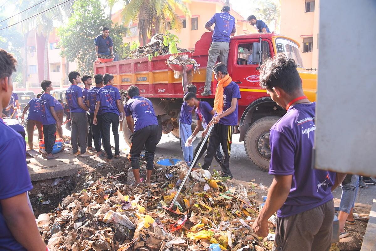 Volunteers clear garbage dumped beside the road near the Mangaluru Central Railway Station on Sunday.