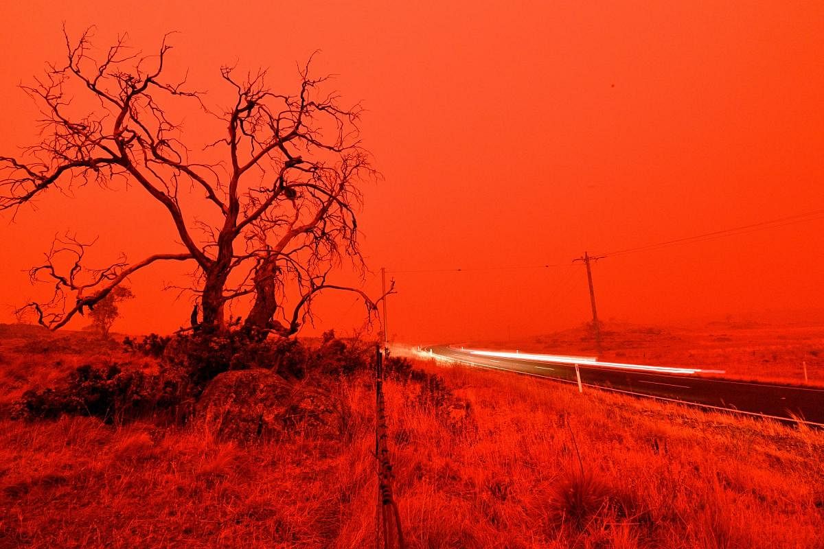 A long exposure picture shows a car commuting on a road as the sky turns red from the smoke of the Snowy Valley bushfire on the outskirts of Cooma. (AFP PHOTO)