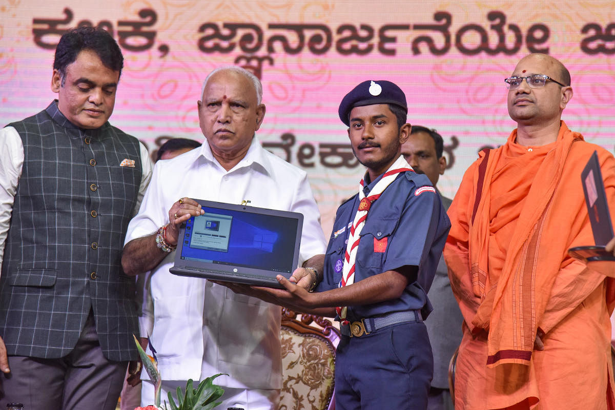 Chief Minister B S Yediyurappa hands over a laptop to a student during the launch of free laptop scheme on the occasion of National Youth Day in Bengaluru on Sunday. Deputy Chief Minister C N Ashwath Narayan and Mangalanathananda Swami of Ramakrishna Mutt