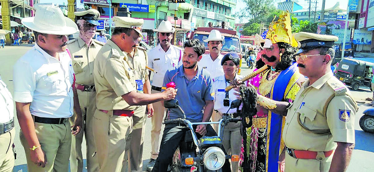 Police personnel handover a rose to a traffic violator during an awareness programme organised as a part National Road Safety Week in Kushalnagar on Sunday.