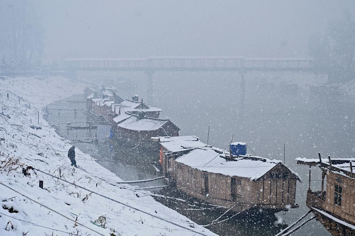 A man walks towards by house boats on the banks of the River Jhelum during snowfall in Srinagar. (AFP Photo)