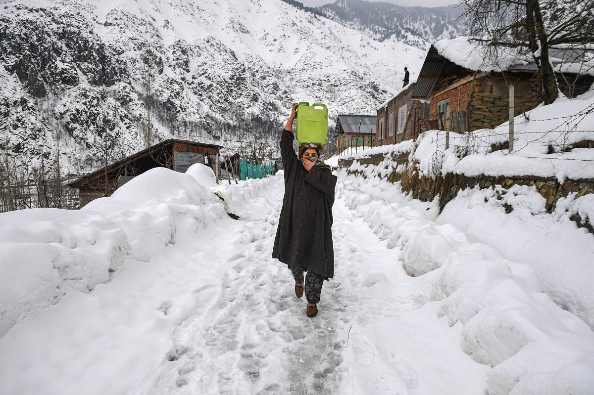 A woman, carrying drinking water, walks on a snow-covered road after heavy snowfall, on the outskirts of Srinagar (PTI Photo)
