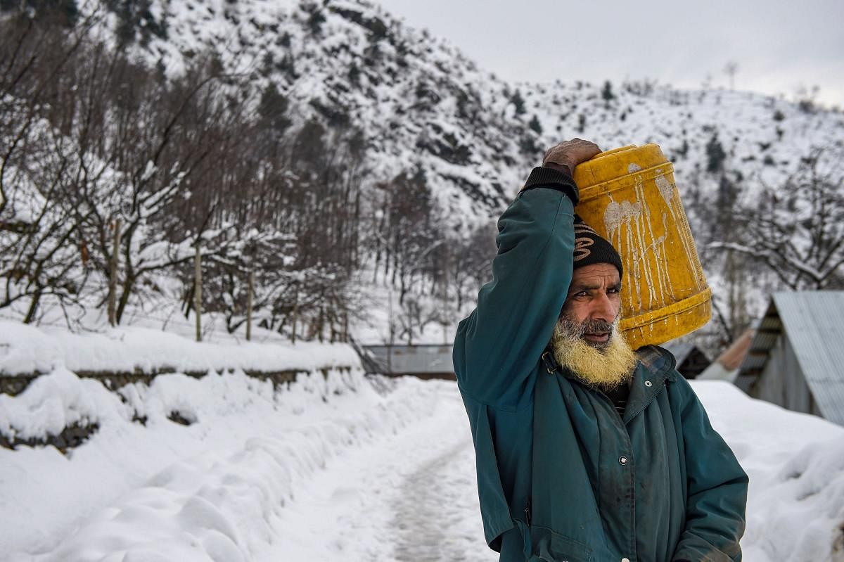 An elderly man, carrying drinking water, walks on a snow-covered road after heavy snowfall, on the outskirts of Srinagar, Tuesday, Jan. 14, 2020. (PTI Photo)