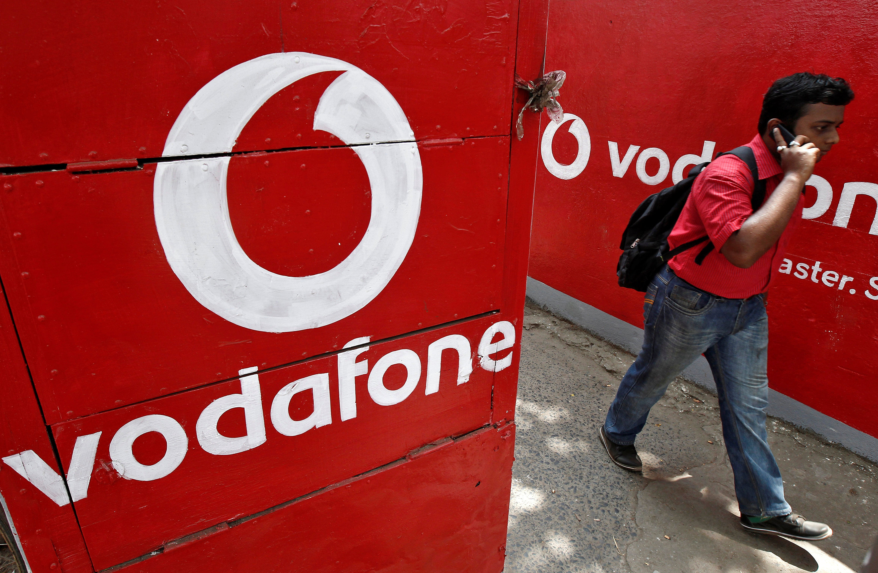  A man speaks on his mobile phone as he walks past logos of Vodafone painted on a roadside wall in Kolkata, May 20, 2014. (Reuters Photo)