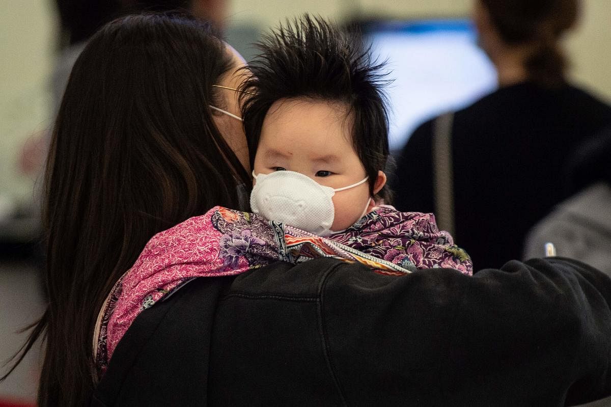 A woman holds a child wearing a facemask as they queue at the West Kowloon rail station in Hong Kong on January 23, 2020. (AFP Photo)