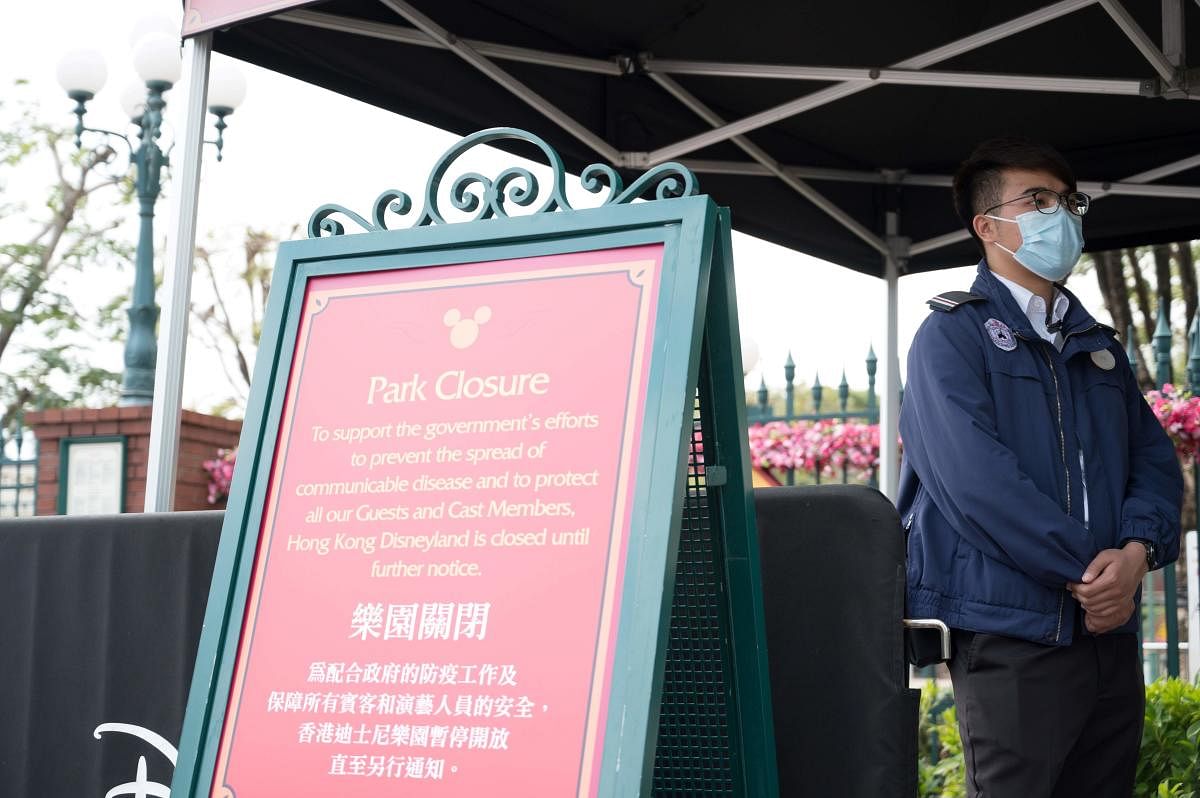 A member of staff wearing a mask stands next to a sign announcing the park's closure at Hong Kong Disneyland in Hong Kong on January 26, 2020, after it announced it was shutting its doors until further notice over a deadly virus outbreak in central China.