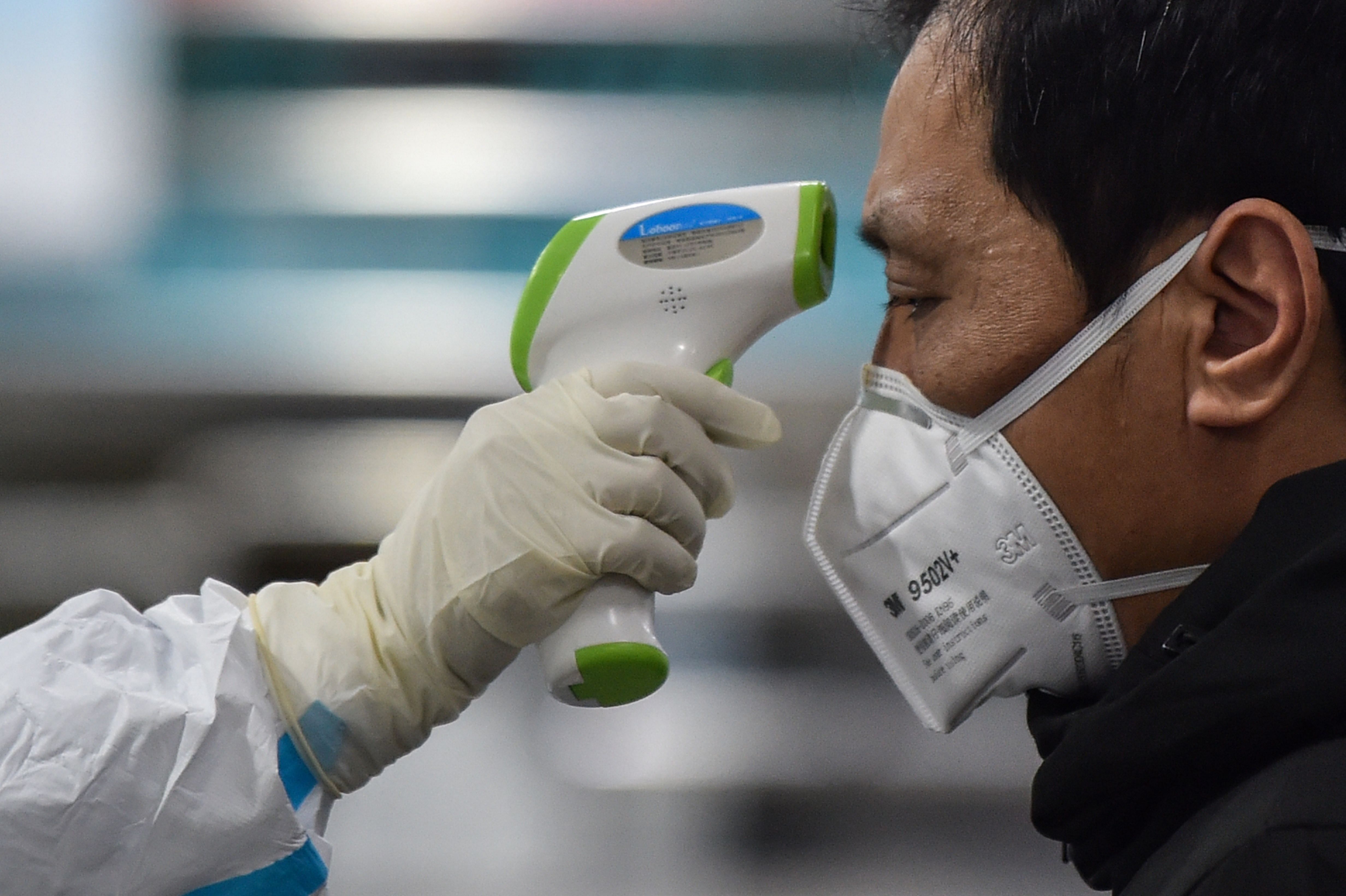 A medical staff member (L) wearing protective clothing to help stop the spread of a deadly virus which began in the city, takes the temperature of a man (R) at the Wuhan Red Cross Hospital. (AFP Photo)