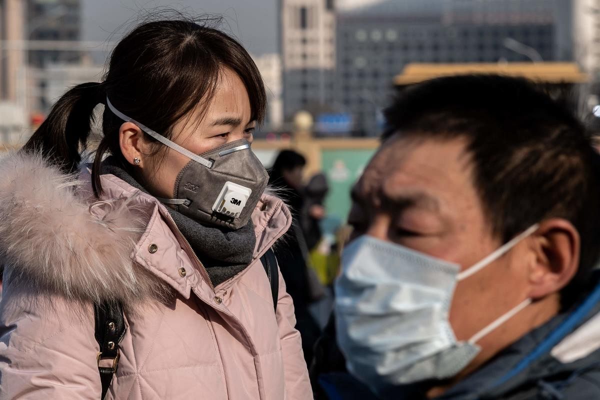 A woman wearing a protective mask walks past a paramilitary police officer (R) outside Beijing railway station in Beijing on January 21, 2020. Credit: AFP Photo