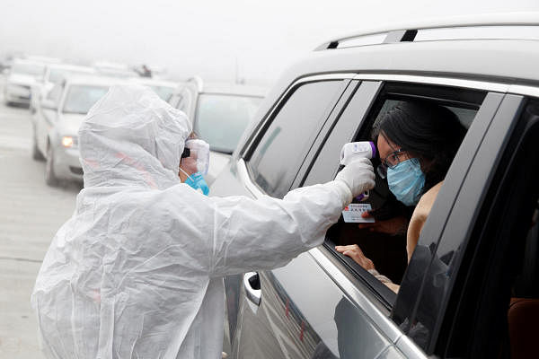 A medical worker in protective suit checks the body temperature of a car passenger at a checkpoint outside the city of Yueyang (Reuters Photo)