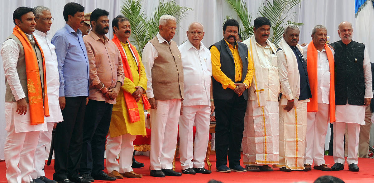 (L-R) K Sudhakar, Shrimant Patil, Ramesh Jarkiholi, Anand Singh, Narayana Gowda, Karnataka Governor Vajubhai Vala and Chief Minister BS Yeddiyurappa, BC Patil, K Gopalaiah, ST Somashekar, Byrathi Basavaraj and Shivaram Hebbar pose for a photo-op after the newly-inducted ministers took oath at Raj Bhavan in Bengaluru on Thursday. | DH Photo: Pushkar V