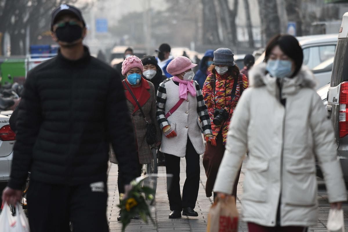 People wear protective face masks as they walk near a market in Beijing (AFP Photo)