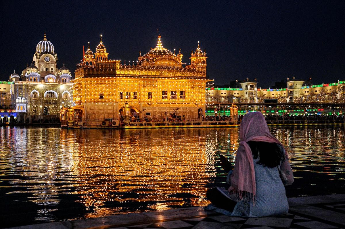 A devotee sits in the backdrop of the illuminated Golden Temple on the eve of 550th birth anniversary of Guru Nanak Dev Ji, founder of the Sikh religion, in Amritsar, Monday, Nov. 11, 2019. (PTI Photo)