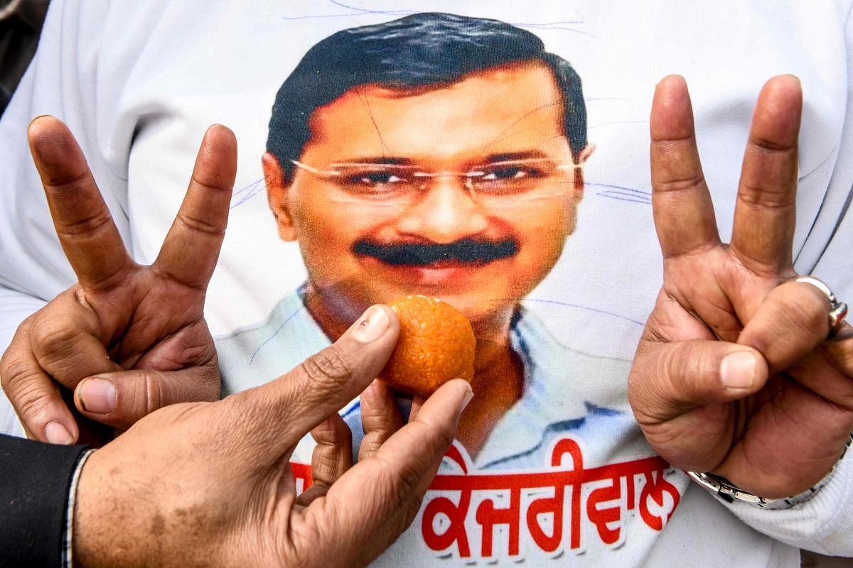 Aam Aadmi Party (AAP) workers offer sweets to eachother as one of them wears a t-shirt showing the face of AAP chief Arvind Kejriwal to celebrate victory following the early results of New Delhi regional assembly election, in Amritsar on February 11, 2020