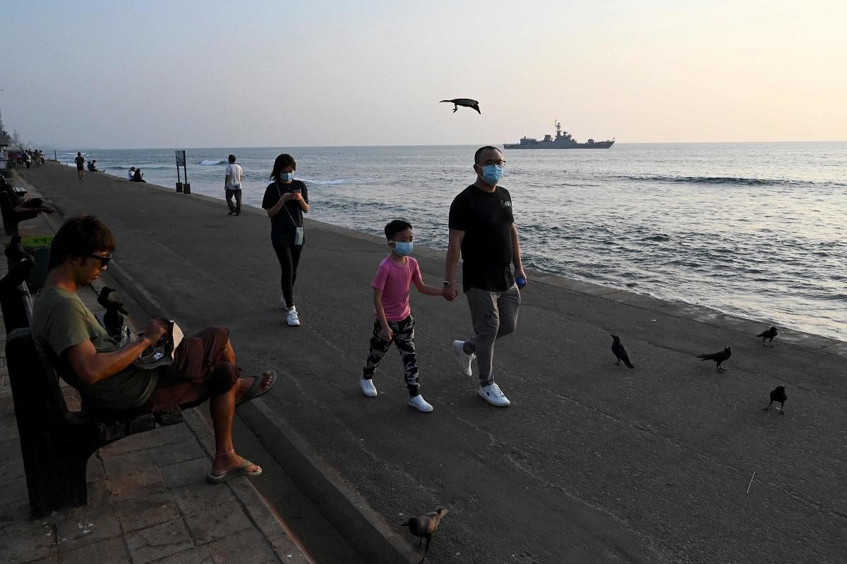 Tourists wearing protective face masks to help stop the spread of a deadly virus which began in Wuhan, walk along Galle Face Green promenade in Colombo. (AFP Photo)