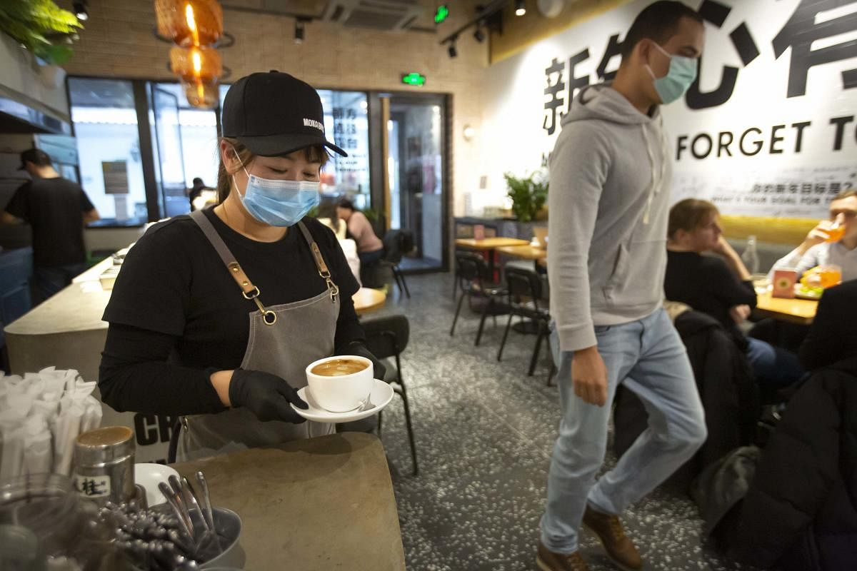 A server wearing a face mask carries a cup of coffee at a Moka Bros cafe in Beijing, Friday, Feb. 14, 2020. (AP Photo)