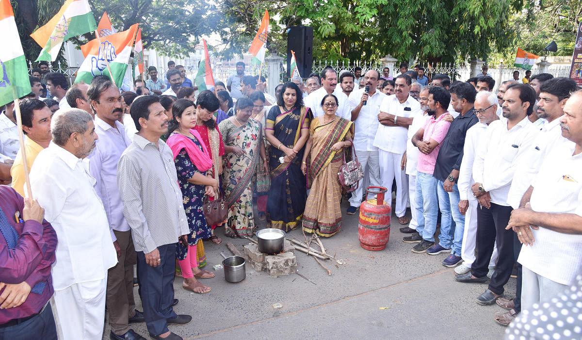 Congress workers cook using firewood, in protest against the rise in the price of LPG cylinders, in front of the taluk panchayat building in Mangaluru on Saturday.
