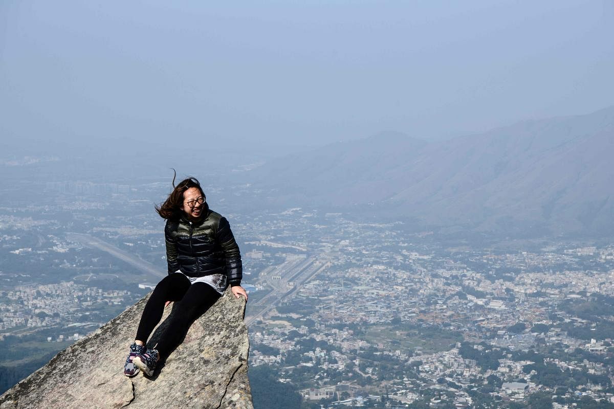 This picture taken on December 8, 2017 shows a woman posing on a rock for photos on Hong Kong's highest peak Tai Mo Shan. Wooded hillsides, craggy ridges and wheeling birds of prey are a world away from Hong Kong's famous skyscrapers but the city's country parks are a necessary balm for its stressed out residents. / AFP PHOTO / Anthony WALLACE / TO GO WITH Hong Kong-lifestyle-environment-nature-hiking-running, FEATURE by Laura MANNERING