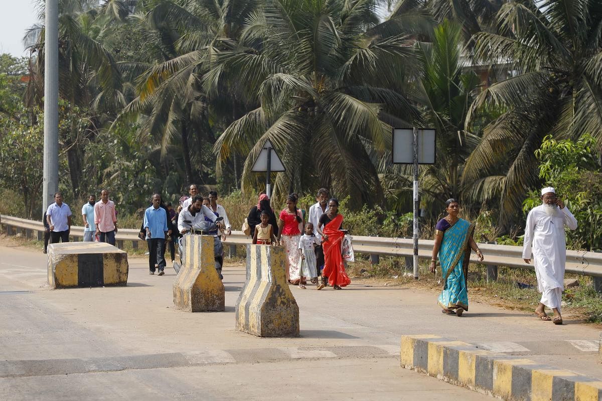 Passengers walk to board a bus in front of the toll gate in Talapady.