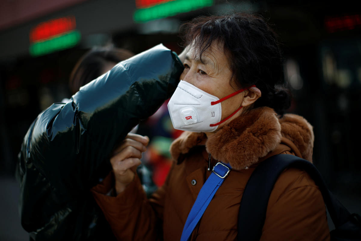 A woman gets help to fit her face mask outside Beijing Railway Station as the country is hit by an outbreak of the new coronavirus, in Beijing. (Reuters Photo)