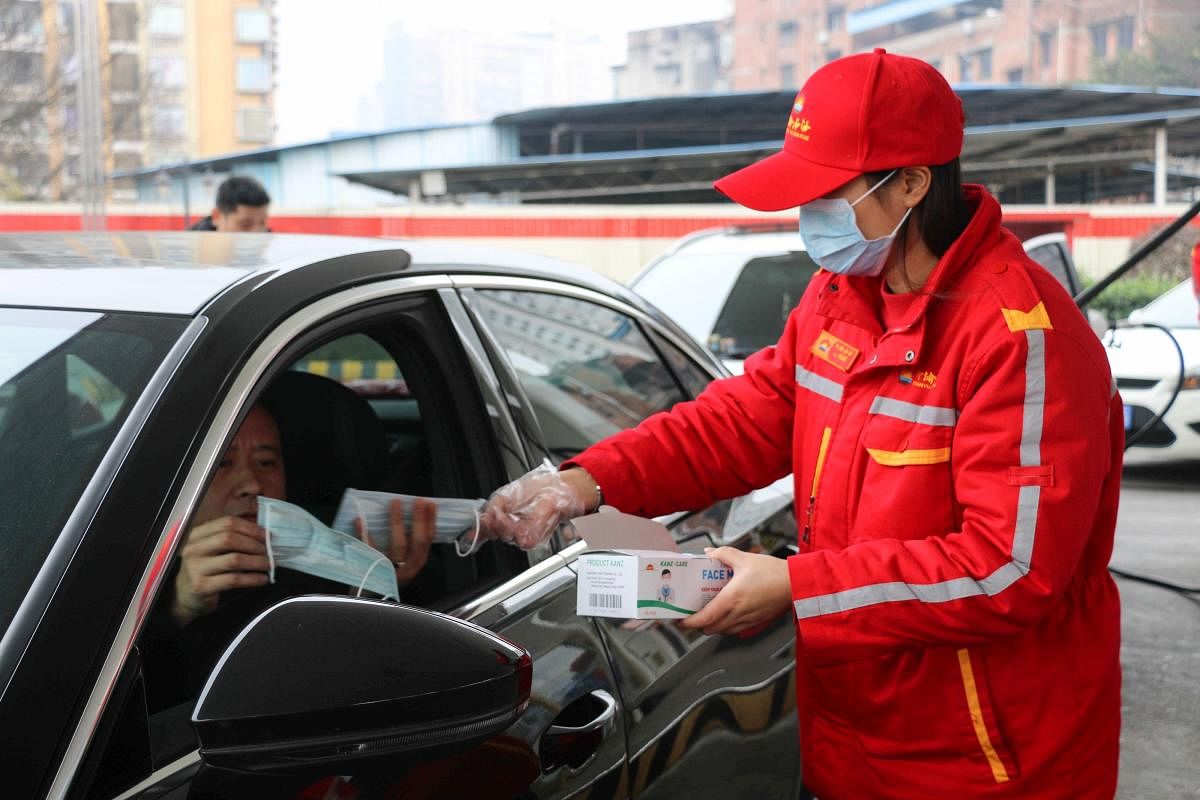 An attendant (R) offers free protective masks to a driver at a gas station in China's southwestern Chongqing on January 23, 2020. Reuters