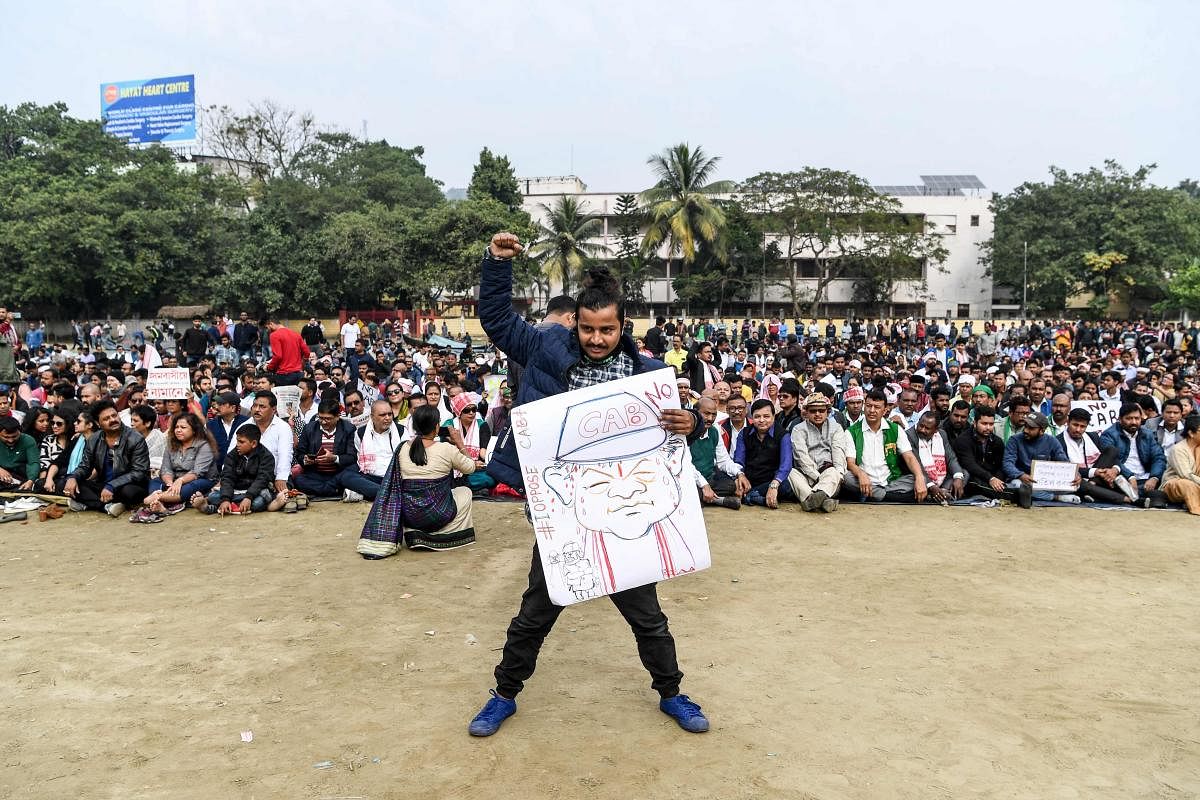 A demonstrator (C) holds a placard displaying a drawing of Assam Chief Minister Sarbananda Sonowal as others sit in the background during a protest against the government's Citizenship Amendment Bill (CAB) in Guwahati. (AFP Photo)