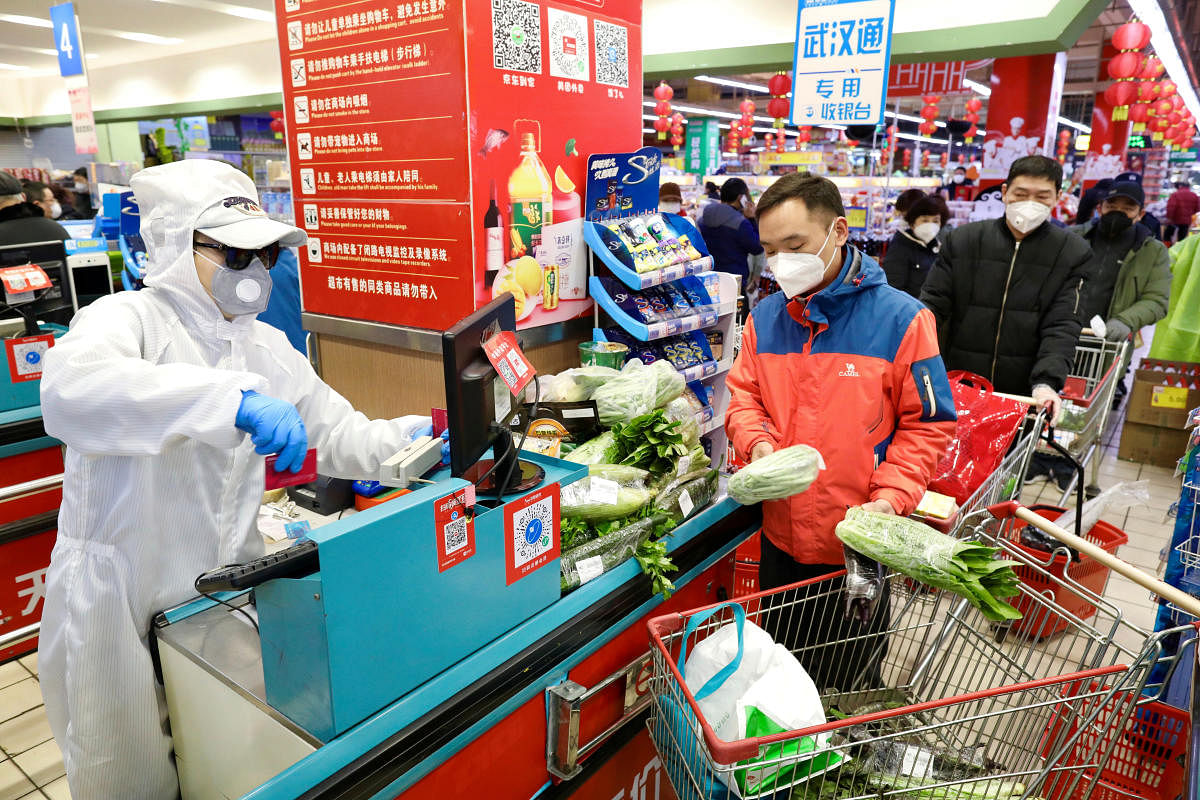 Worker in protective suit serves customers at a checkout counter of a supermarket following the outbreak of the novel coronavirus in Wuhan. Credit: Reuters Photo