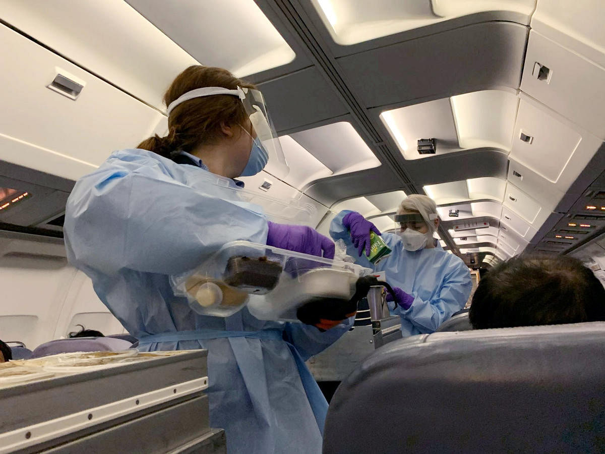 Flight attendants wearing protective clothing and masks serve snacks to Canadians, who had been evacuated from China due to the outbreak of novel Coronavirus on an American charter plane, on another aircraft taking them to Canadian Forces Base (CFB) Trent