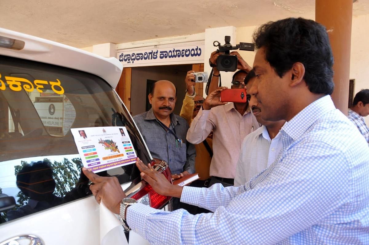 Deputy Commissioner Dr Bagadi Gautham pastes a sticker on 'Chikkamagaluru Habba' on a vehicle in Chikkamagaluru on Friday.
